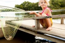 Girl on jetty with frog in fishing net — Stock Photo