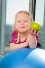 Chica comiendo manzana en la pelota de ejercicio - foto de stock