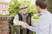 Senior man and mid adult man shaking hands over gate — Stock Photo