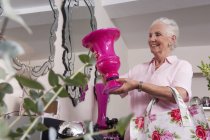 Senior woman holding up vase in florist shop — Stock Photo