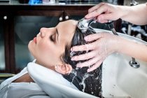 Женский парикмахер полоскает волосы молодой клиентки в салоне — стоковое фото