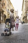 Mãe e filha pulando na rua enquanto empurrava a carruagem do bebê, Bolonha, Itália — Fotografia de Stock