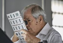Homem sênior olhando para a folha de slides de filme com lupa — Fotografia de Stock