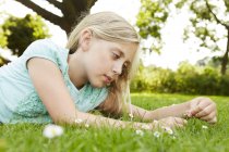 Дівчина лежить на траві дивиться на ромашку — стокове фото