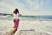 Visão traseira da mulher de pé em ondas de surf na praia — Fotografia de Stock