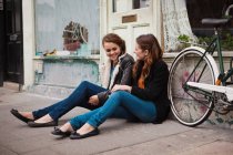 Duas jovens mulheres sentadas no chão do lado de fora do café — Fotografia de Stock