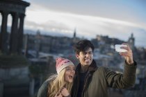 A young couple photograph themselves on Calton Hill with the background of the city of Edinburgh, capital of Scotland — Stock Photo