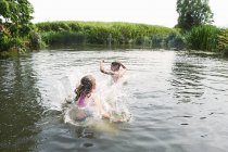 Adolescente y hermana chapoteando en el lago rural - foto de stock