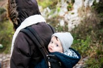 Portrait of baby boy wearing knit hat, carried in baby sling by mother — Stock Photo