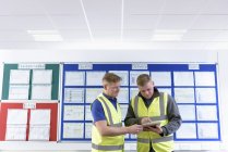 Ingénieurs avec tablette numérique devant la carte de productivité et de sécurité dans l'usine d'ingénierie — Photo de stock