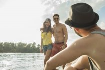 Молода пара стоїть на озері і розмовляє з другом — стокове фото