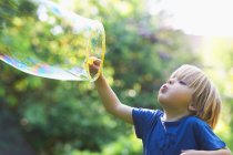 Boy blowing oversized bubble in backyard — Stock Photo