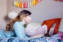Young woman lying on shabby chic bed looking at laptop — Stock Photo