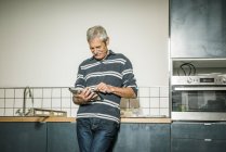 Senior man using digital tablet in kitchen — Stock Photo