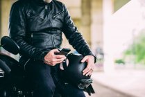Середній розділ дорослого чоловіка мотоцикліста, що сидить на мотоциклі смс на смартфоні — стокове фото