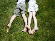 Overhead view of brother and sisters legs as they lay on grass — Stock Photo