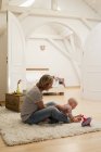 Mature mother and baby daughter playing on rug in sitting room — Stock Photo