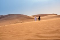 Distant view of couple wearing traditional middle Eastern clothes walking on desert dune, Dubai, Emirati Arabi Uniti — Foto stock