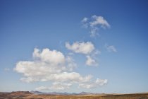 Weiße Wolken am blauen Himmel über hügeliger Landschaft — Stockfoto