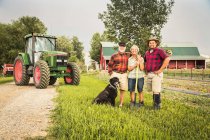 Сім'я з собакою на фермі перед трактором дивиться на камеру посміхаючись — стокове фото