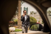 Vue de fenêtre de voiture de l'homme d'affaires parlant sur smartphone à l'extérieur de l'hôtel, Dubaï, Émirats arabes unis — Photo de stock