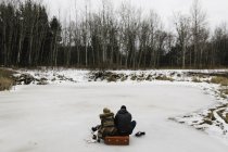 Пара сидящих на красном чемодане посреди замёрзшего озера, Уитби, Онтарио, Канада — стоковое фото