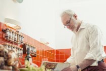 Старший мужчина готовит дома на кухне — стоковое фото
