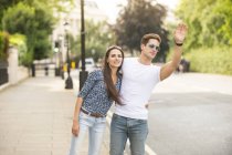 Young couple hailing a cab on city street, London, UK — Stock Photo