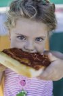 Girl eating slice of pizza and looking in camera, portrait — Stock Photo
