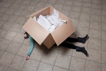High angle view of teenage girl lying under cardboard box — Stock Photo