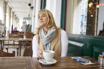 Femme mûre regardant sur le trottoir table de café — Photo de stock