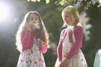 Duas meninas bonitos soprando bolhas no jardim iluminado pelo sol — Fotografia de Stock