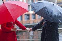 Symmetrical couple holding handrail and carrying umbrella's — Stock Photo