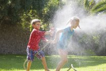 Boy splashing girl in garden with water sprinkler — Stock Photo