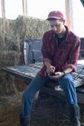 Jeune agriculteur assis et utilisant un téléphone portable — Photo de stock