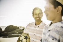 Отец несет футбол с сыном на пляже — стоковое фото