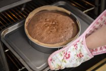 Gros plan des mains féminines retirant le gâteau du four dans la boulangerie — Photo de stock