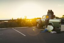 Vue arrière du couple à l'arrière d'une camionnette regardant le coucher du soleil à Newport Beach, Californie, États-Unis — Photo de stock