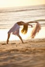 Young woman dancing on sunlit beach — Stock Photo