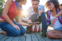 Young women and man using digital tablet on decking — Stock Photo