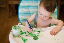 Baby boy sitting in high chair painting picture — Stock Photo