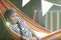 Portrait de fille mignonne avec bandeau et tresse inclinable dans un hamac de jardin rayé — Photo de stock