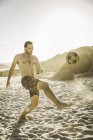 Mid adult man wearing swimming shorts playing soccer on beach, Cape Town, South Africa — Stock Photo