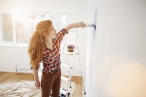 Рыжая девушка-подросток в шашечной рубашке рисует стену спальни — стоковое фото