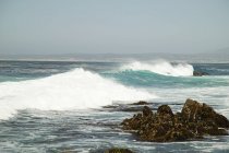 Onde che colpiscono rocce sulla spiaggia nuvolosa — Foto stock