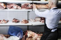 Butcher placing joint of meat on refrigerated cabinet, rear view — Stock Photo