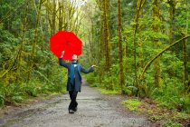 Femme sur le sentier forestier avec parapluie rouge — Photo de stock