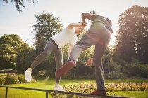 Homem de mãos dadas com personal trainer equilibrando em uma perna na cerca do parque — Fotografia de Stock