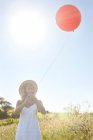 Uma menina em um campo com um balão vermelho — Fotografia de Stock