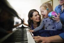 Padres enseñando a su hija a tocar piano - foto de stock